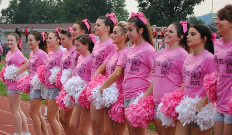 The cheerleaders wear pink shirts and use pink pom-poms to support breast cancer.