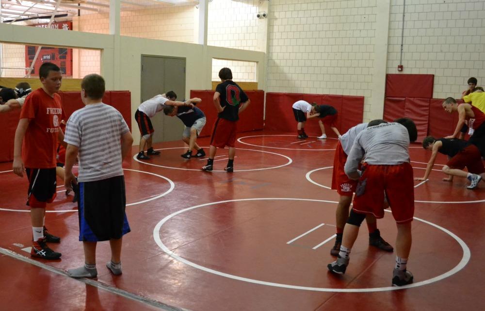 The wrestling team warms up in groups of two by working on technical moves with one another.