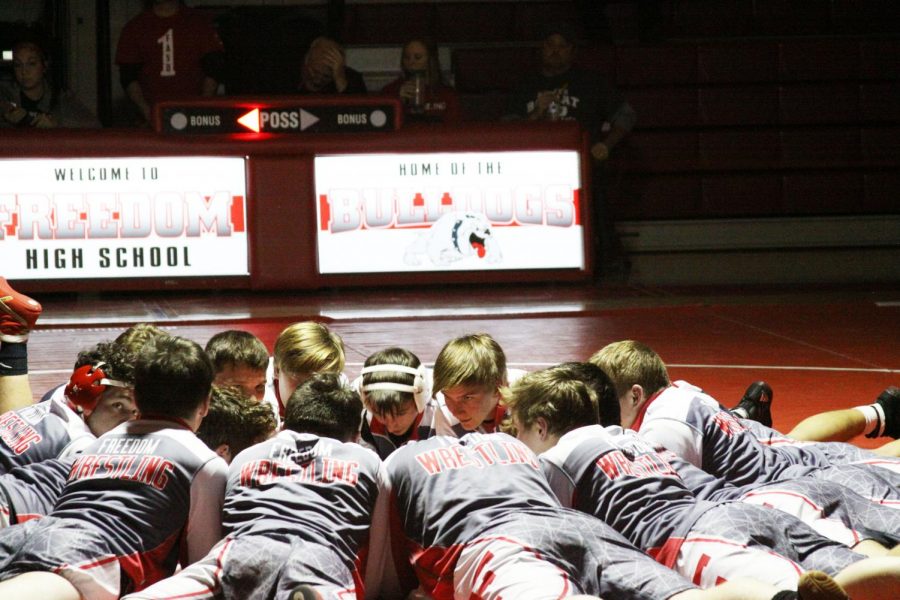 The team meets in the center of the mat for a pep talk before their match.