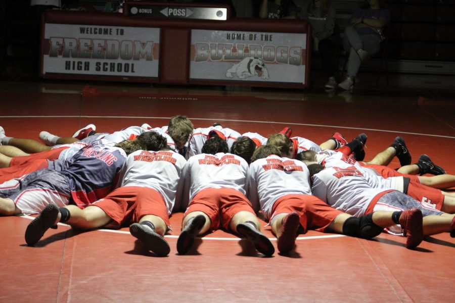 The+wrestlers+circle+up+in+the+middle+of+the+matt+to+get+themselves+ready+before+their+match+on+Dec.+13.