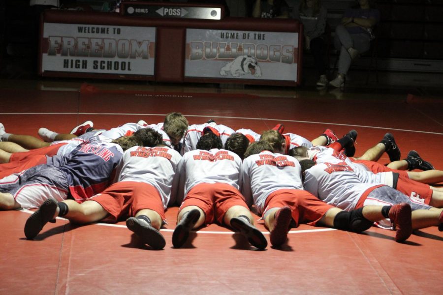 The wrestling team huddles together on the mat for a pep talk as they prepare for their matches.