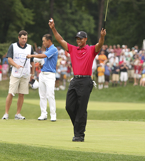 Celebrating sinking his 18th hole shot, Tiger Woods puts his hands and club in the air at the AT&T National Tournament.