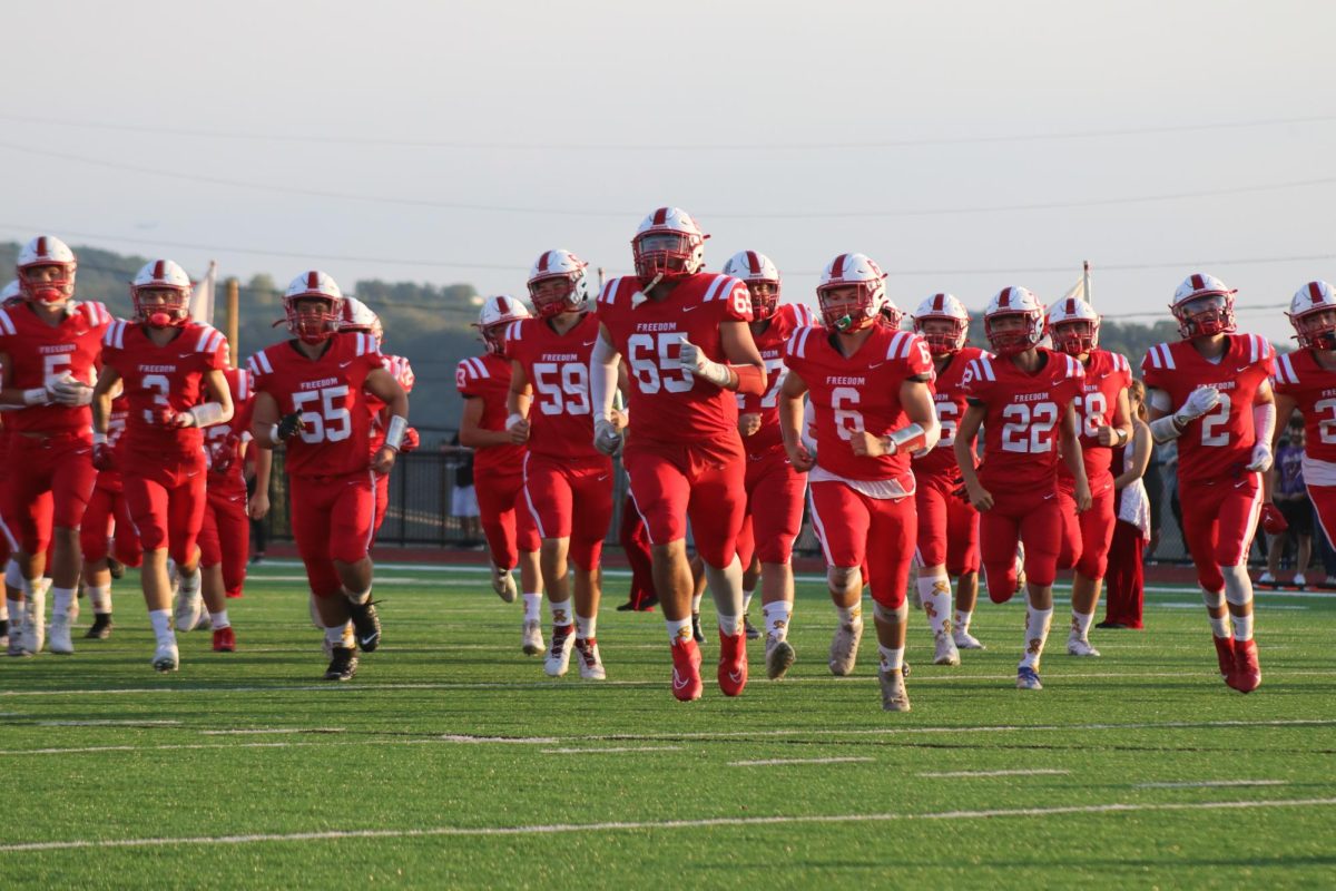Enticing entrance: The varsity football team storms the field after their introduction during the first home game of the season. The team was also joined by all of the younger divisions of Freedom football.
