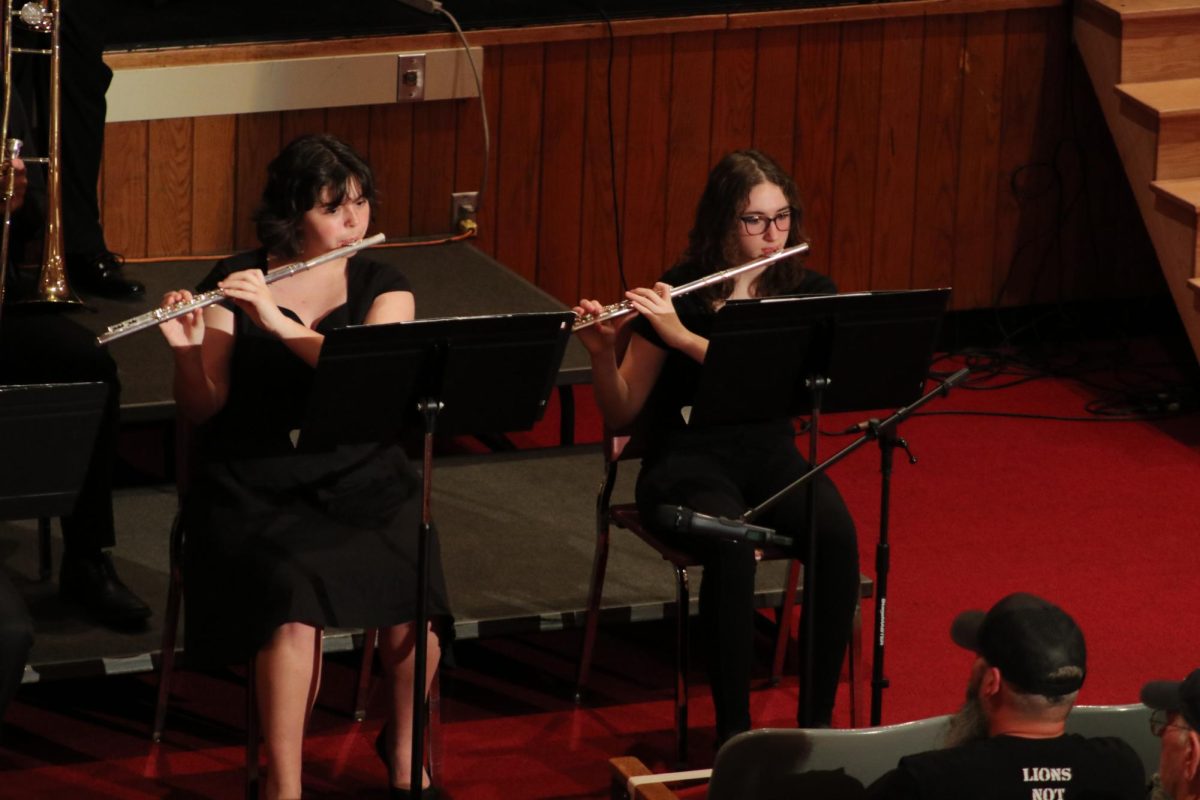Doubling up: Sitting next to each other, senior Lilly Burgess and sophomore Aubrey Boyd read through their jazz band sheet music together at the concert. Being the only two flute players in jazz band, the girls played with a microphone in front of their stands to amplify their instruments for the audience.