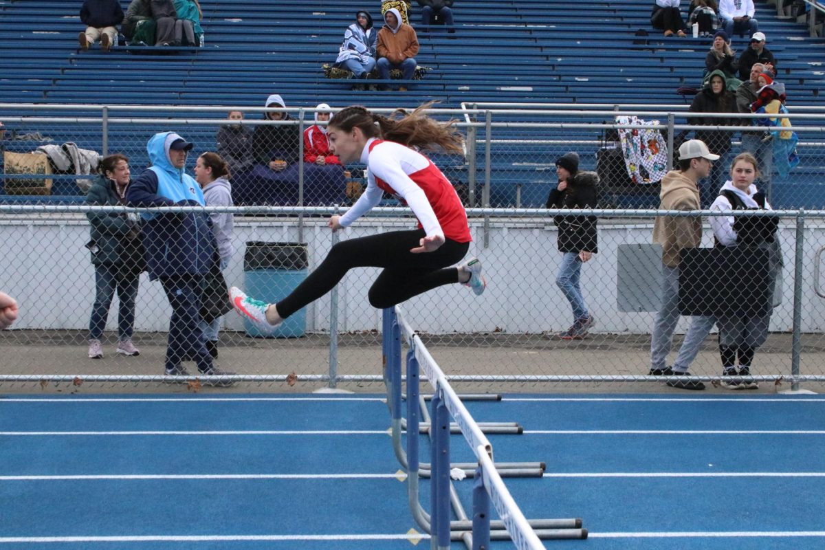 Catching air: Clearing the hurdle, junior Riley Tokar focuses on the track in front of her. If a runner's foot were to catch a hurdle, they are designed to tip over easily to prevent injury.