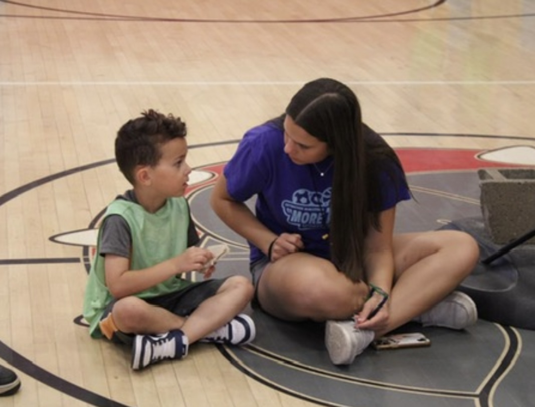 Friendly faces: Spending her break working at the Skybacher “More Than Sports” camps, Farisa Roberts (11) talks to one of the children in her group. Many students enjoy volunteering at these camps as a way to stay productive during the summer.